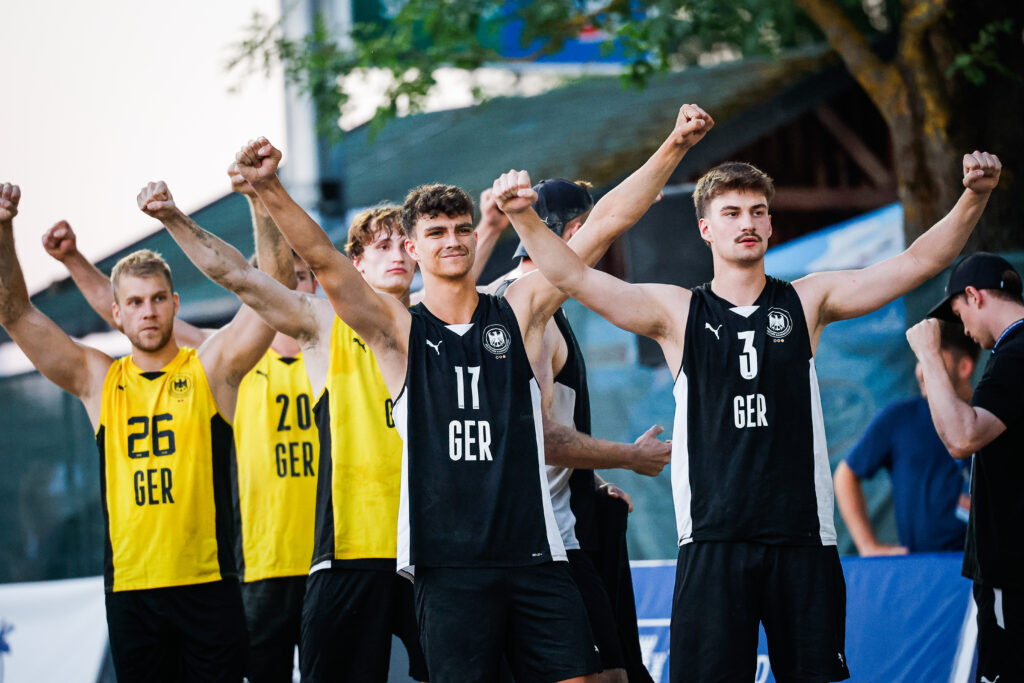 A group of athletes in German national team jerseys raise their fists in unison, displaying unity and determination.