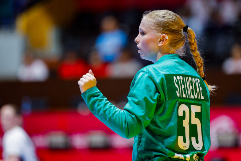 A player in a green jersey with the name "STEINECIE" and number "35" on the back raises her fist in a gesture of determination during a sports event.