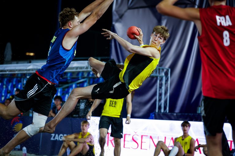 An athlete in a yellow and black uniform leaps mid-air to catch a ball while being defended by an opponent in a blue jersey during a fast-paced game.